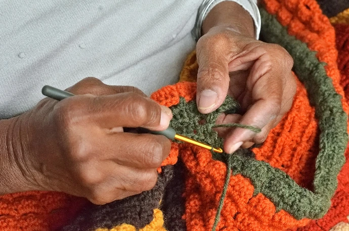 A person is crocheting a blanket with a crochet hook